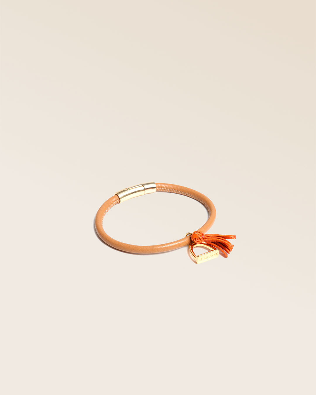 Notre bracelet Jumping en cuir d'agneau camel et pompon orange vu de quart en studio.