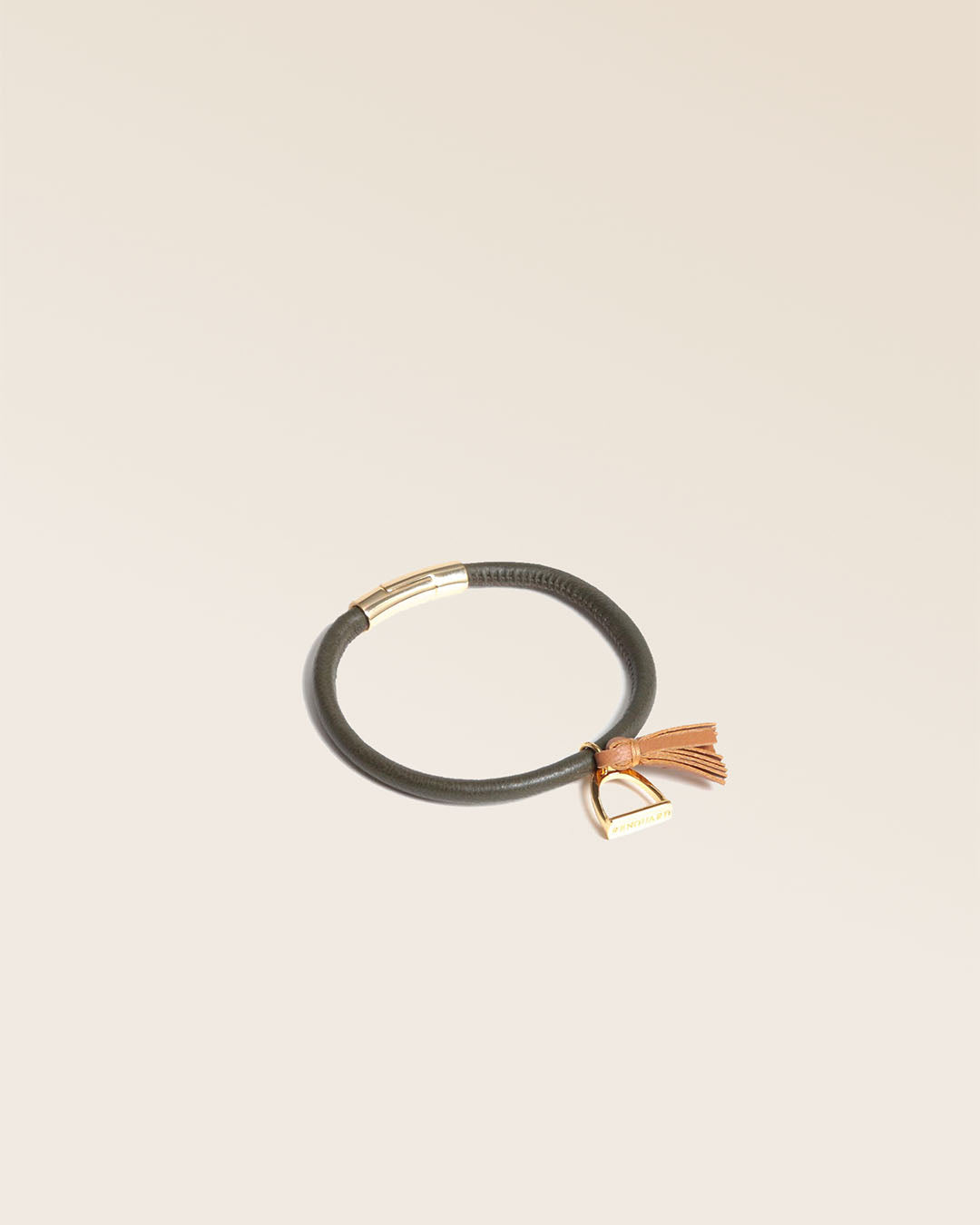 Notre bracelet Jumping en cuir d'agneau kaki et pompon camel vu de quart en studio.