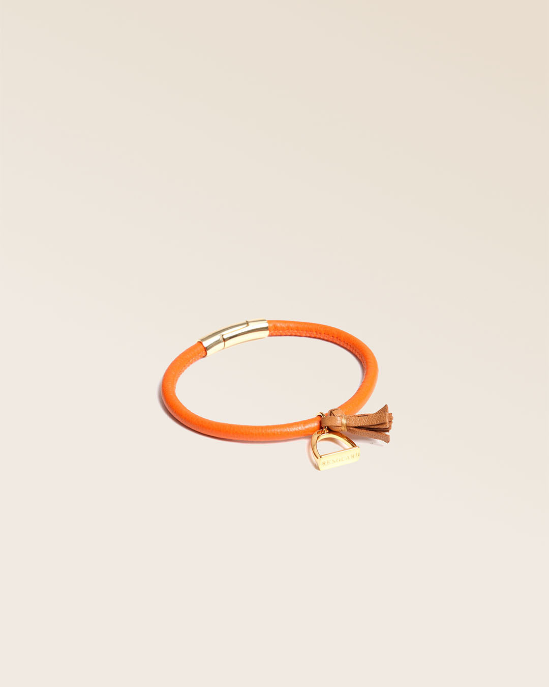 Notre bracelet Jumping Renouard en cuir d'agneau orange et pompon camel, vu de quart en studio.