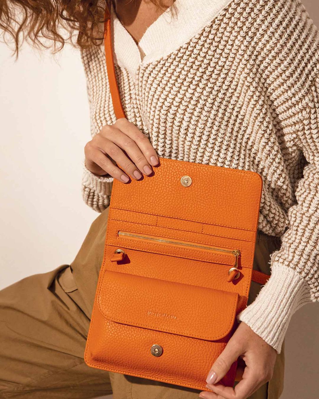 Our Fréhel clutch in orange vicuña-style leather seen from the front worn by our model.