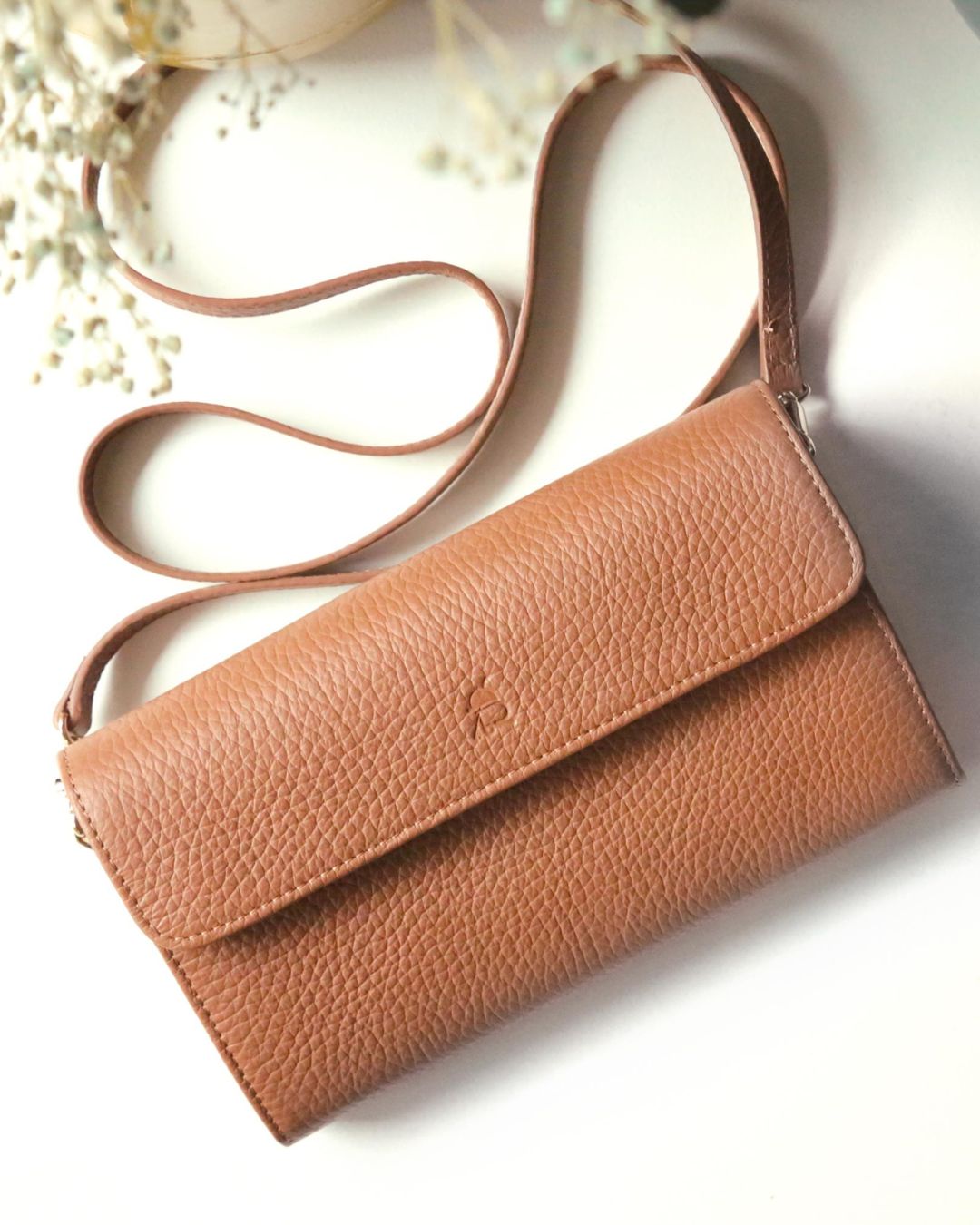 Our Raphaël Renouard clutch in fawn-colored vicuña leather, seen from the front in a floral setting.