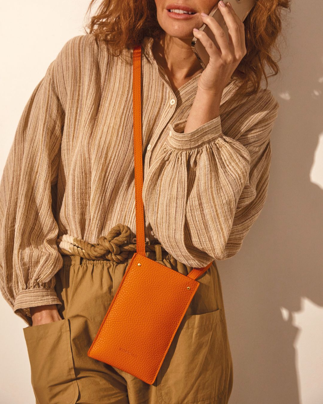 Our Renouard phone pouch in orange vicuña-style leather seen on our model.