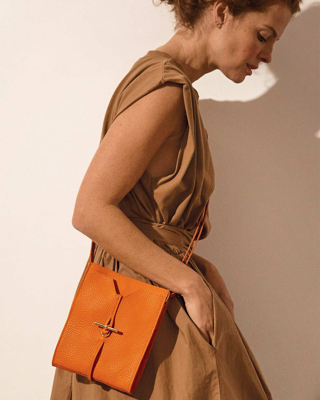 Notre pochette Aglaé Renouard en cuir façon vigogne orange, vue portée par notre mannequin.