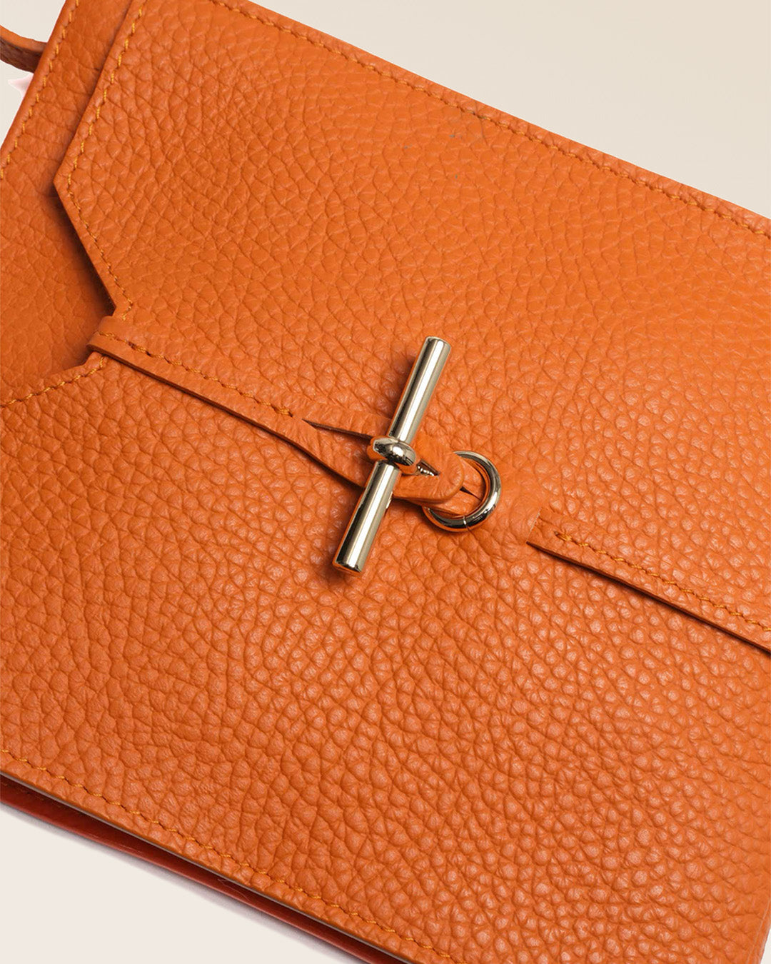 Notre pochette Aglaé Renouard en cuir façon vigogne orange, vue de près en studio.