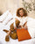 Our Étrivière small bag in orange vicuña-style leather, seen from the front, worn by our model.