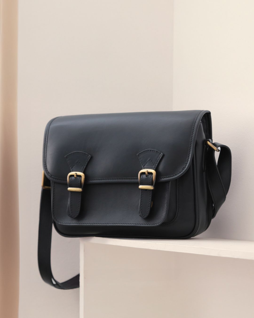 Notre sac Korrigan en cuir lisse noir vu de face, posé sur une étagère.