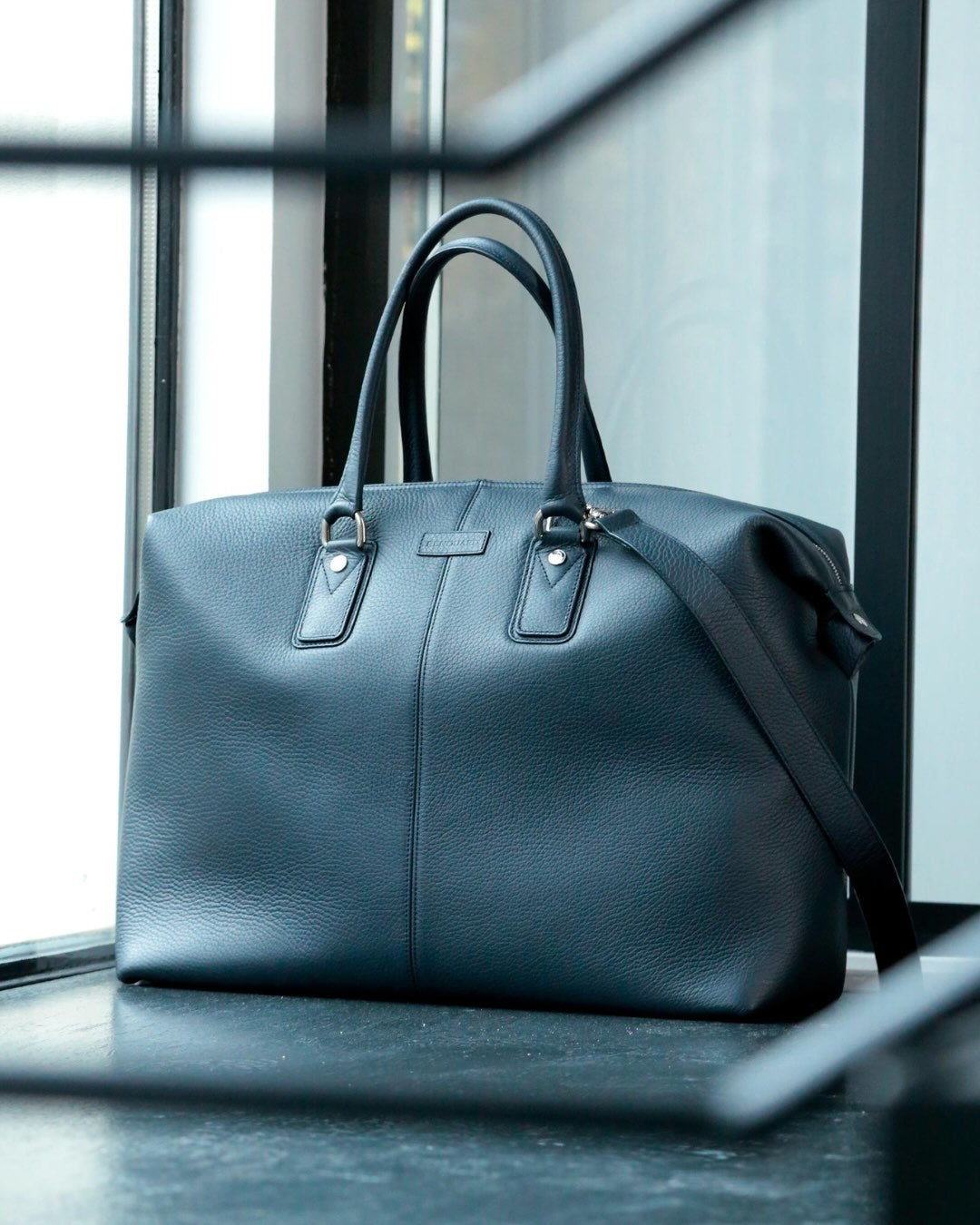 Notre sac de voyage Escapade petit modèle en cuir façon vigogne bleu marine vu de quart en ambiance. #taille_petit