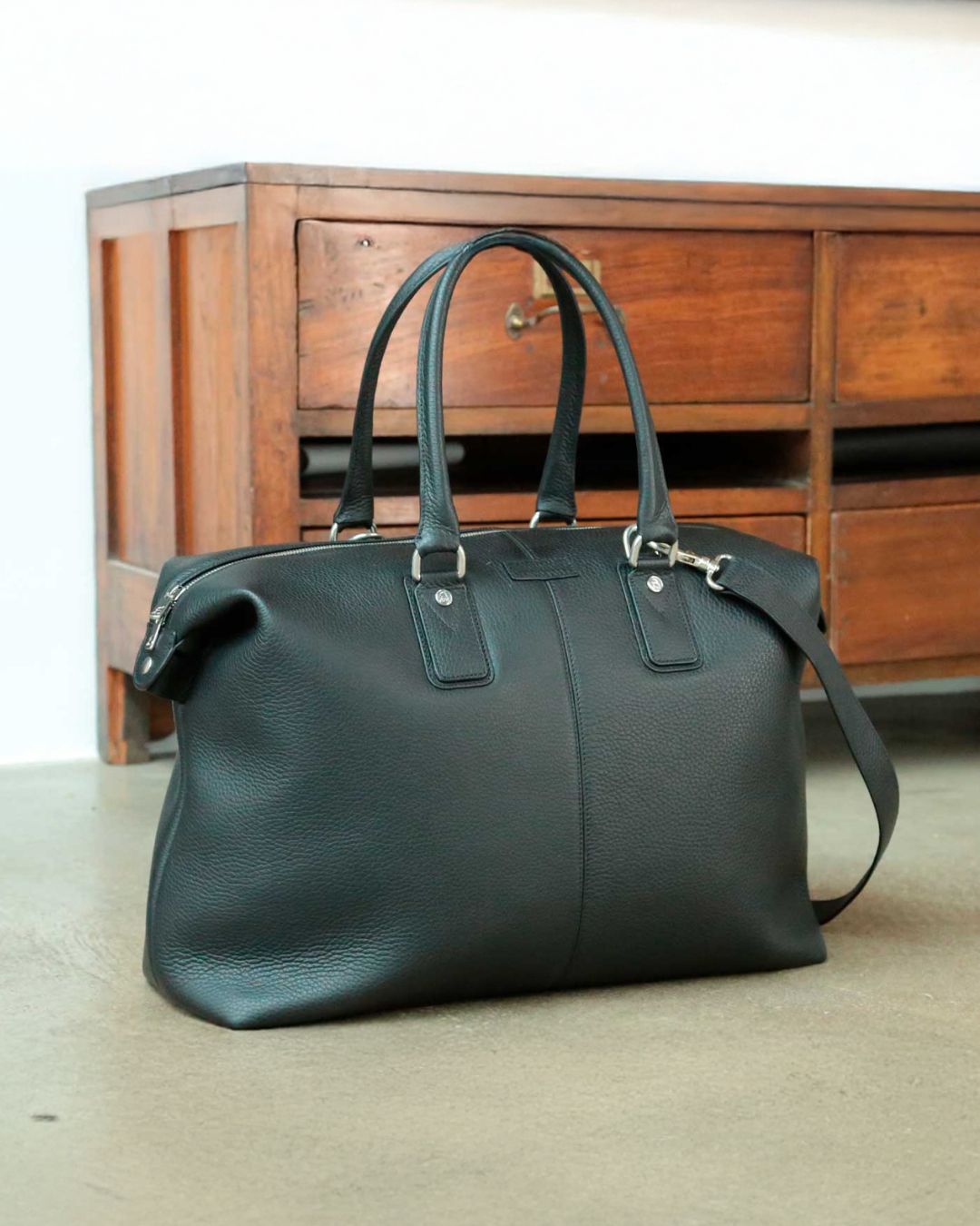 Notre sac de voyage Escapade petit modèle en cuir façon vigogne noir vu de quart en ambiance.
