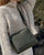 Our Zoom bag in khaki vicuña-style leather and leather shoulder strap as seen from the front, worn by our model.