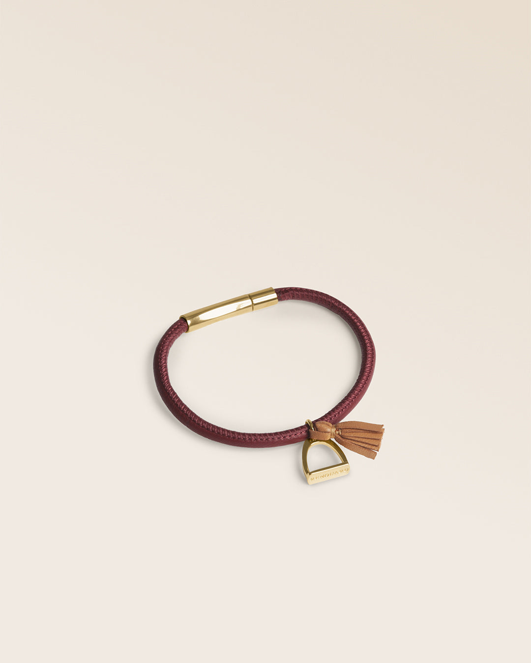 Le bracelet Jumping Renouard en cuir d'agneau lisse bordeaux et son pompon camel, vu de quart en studio.