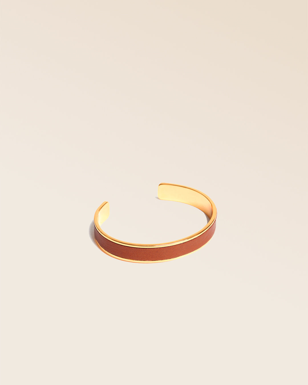 Le bracelet Pacôme Renouard doré et cuir lisse camel, vu de quart en studio.
