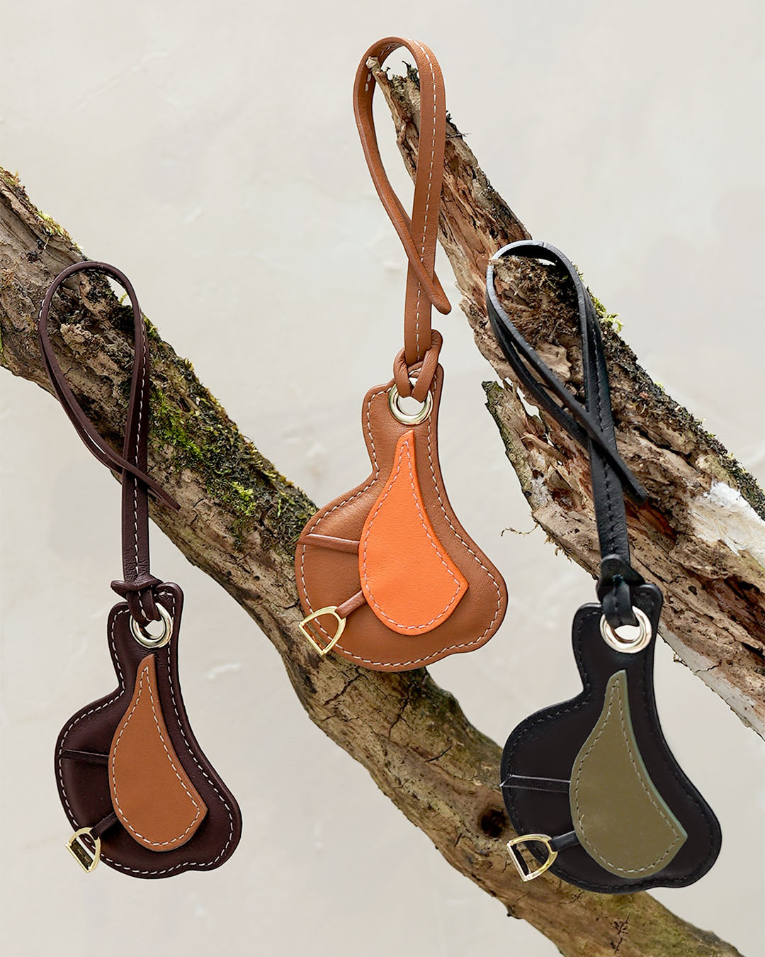 Le bijou de sac Selle Renouard dans ses trois déclinaisons actuelles : cuir lisse camel et orange, cuir lisse noir et truffe, cuir lisse ébène et camel. 