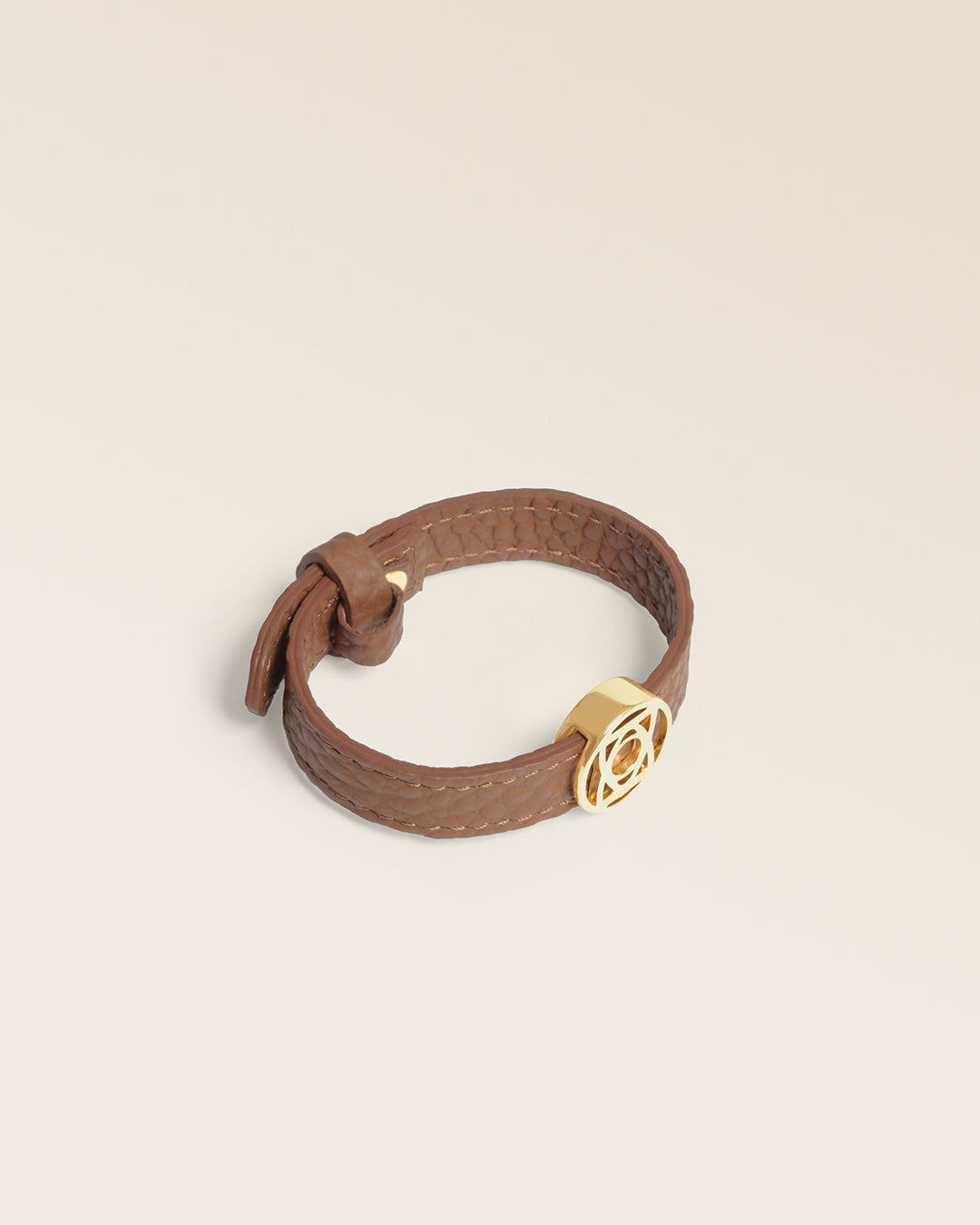 Le bracelet Alezan Renouard en cuir façon vigogne fauve et accessoire doré, vu de quart en studio.