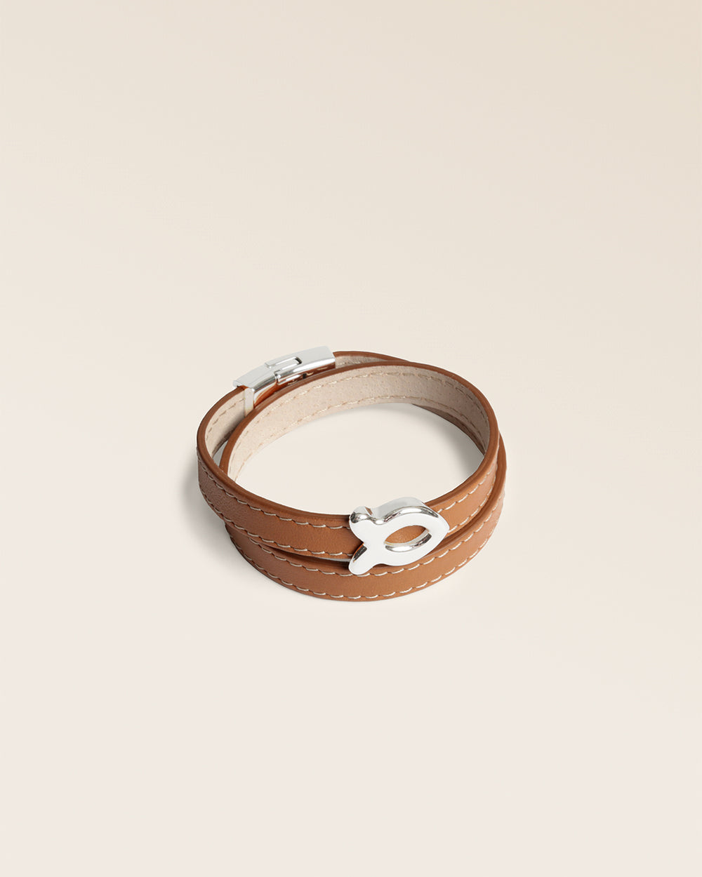 Le bracelet Sardine Renouard en cuir lisse camel et son accessoire poisson nickelé, vu de quart en studio.