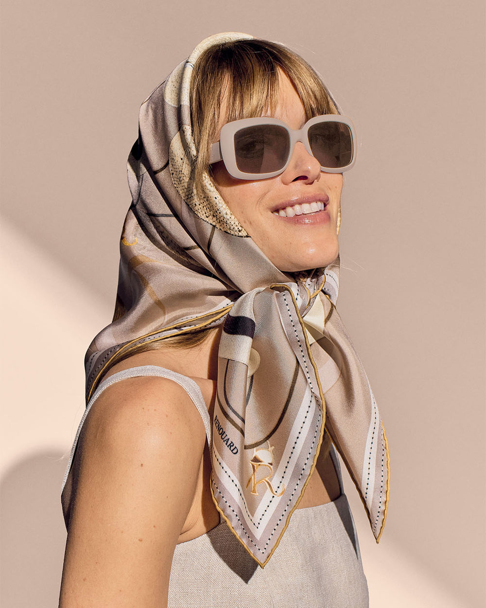 Notre carré de soie Rimbambelle Renouard, dans son coloris beige, vu porté par notre mannequin.