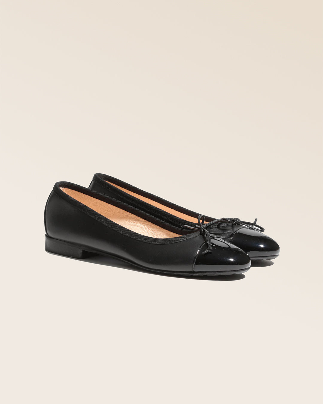 Nos ballerines Friandise Renouard en cuir lisse noir et bout vernis, vues de quart en studio.