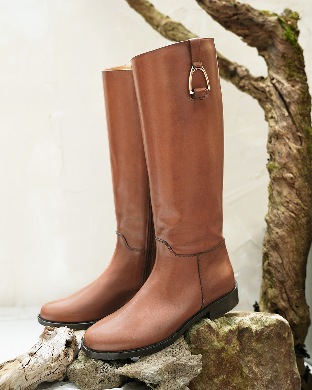Les bottes Horse Renouard en cuir de veau lisse gold et leur accessoire étrier doré pâle, vues de quart en ambiance.