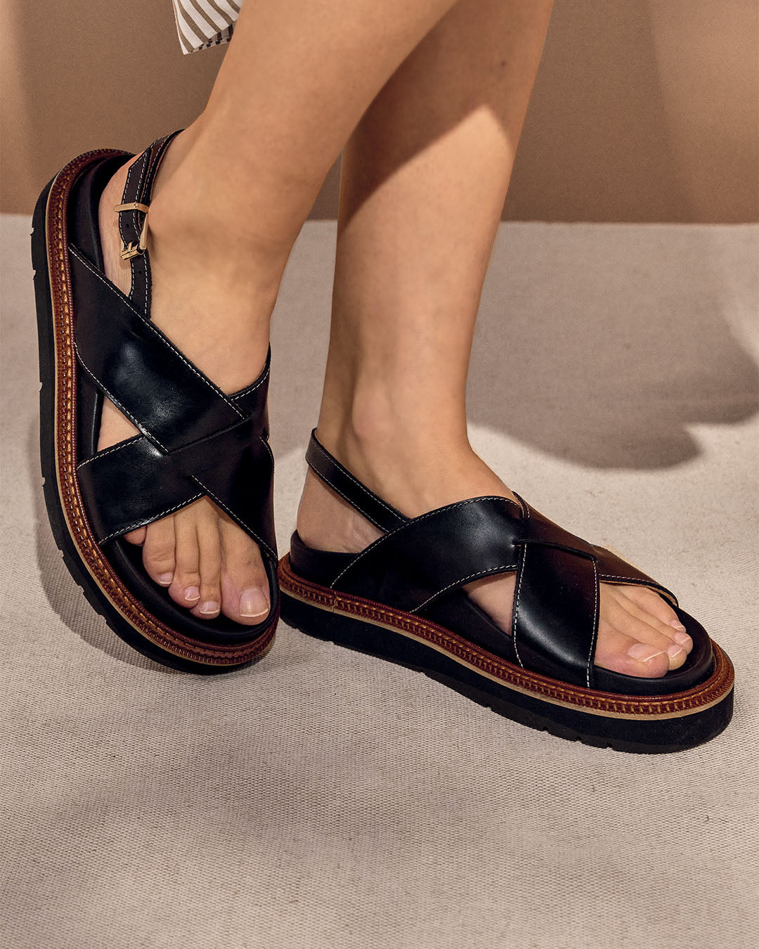 Les nu-pieds Olympe noirs en cuir lisse, vus portés par un mannequin.