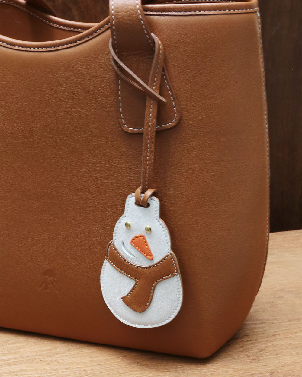 Notre bijou de sac Bonhomme de Neige Renouard, en cuir vintage camel et craie, vu porté sur notre sac Soline. 
