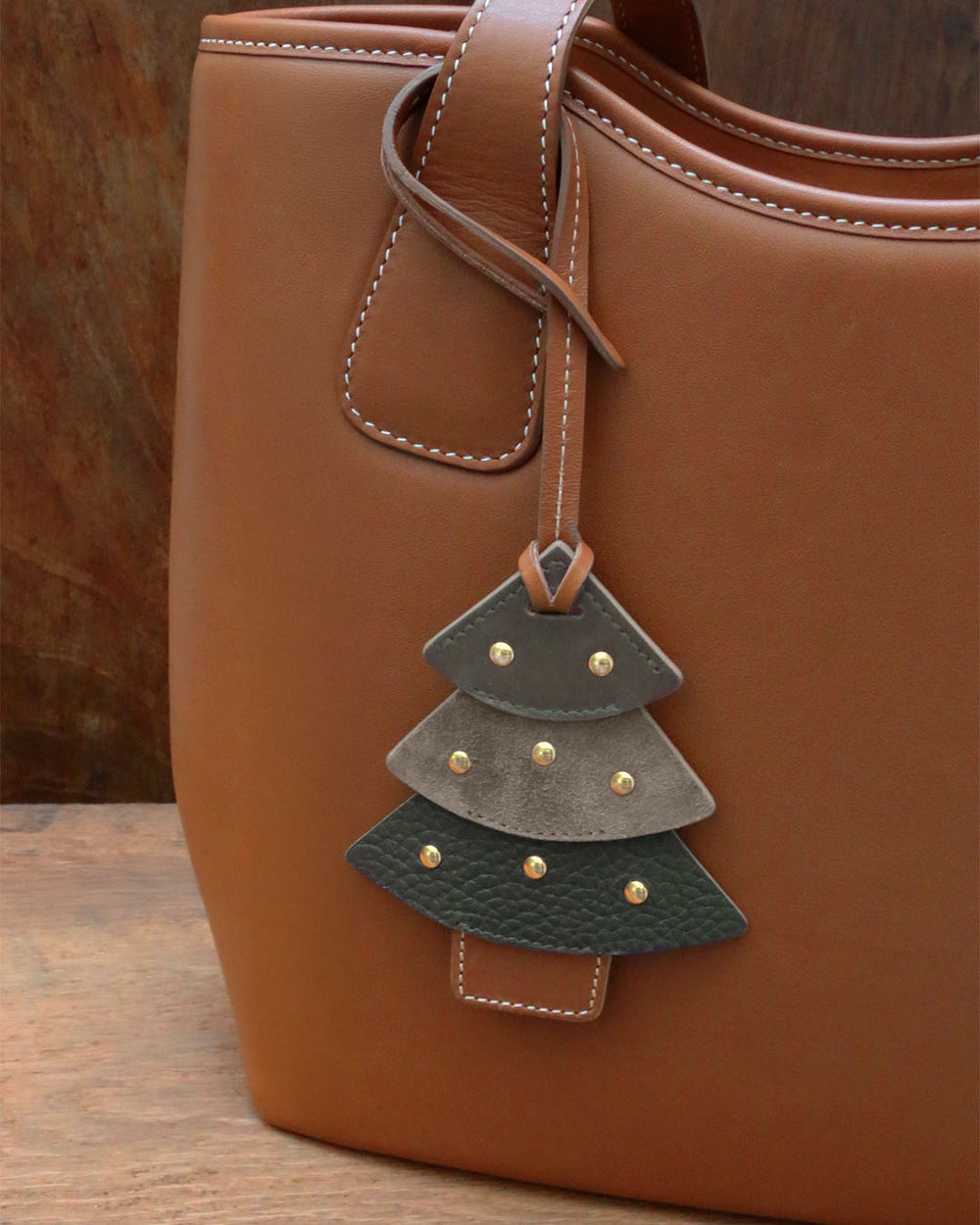 Notre bijou de sac Sapin Renouard, en cuir lisse truffe, veau velours truffe et façon vigogne kaki, vu porté sur notre sac Soline.