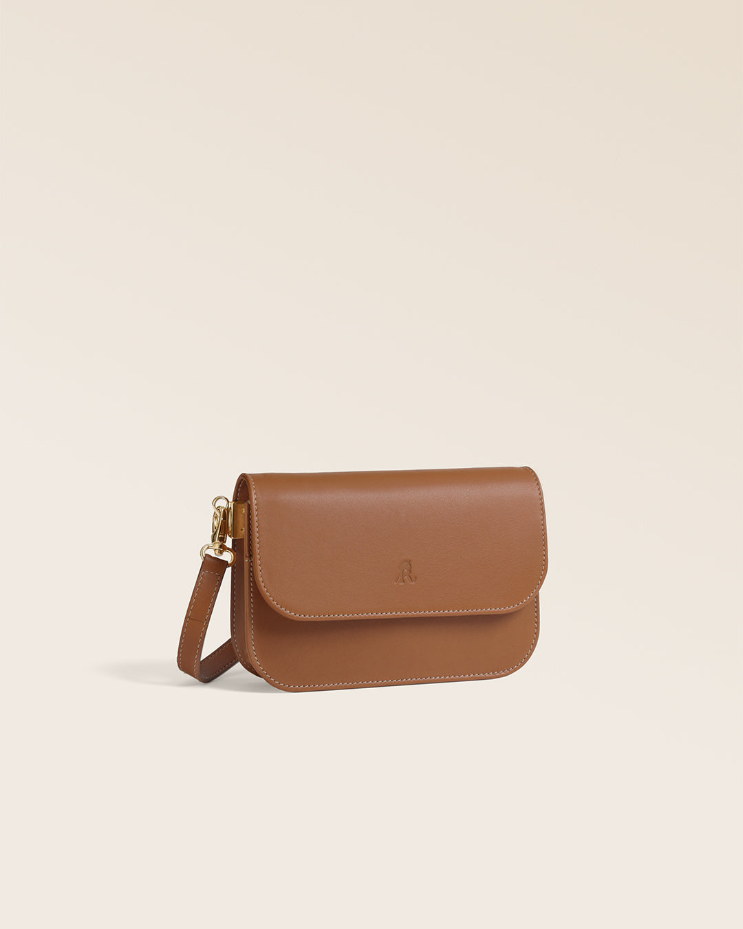 La pochette Coralie Renouard en cuir lisse camel et accessoires dorés, avec sa bandoulière amovible, vue de quart en studio.