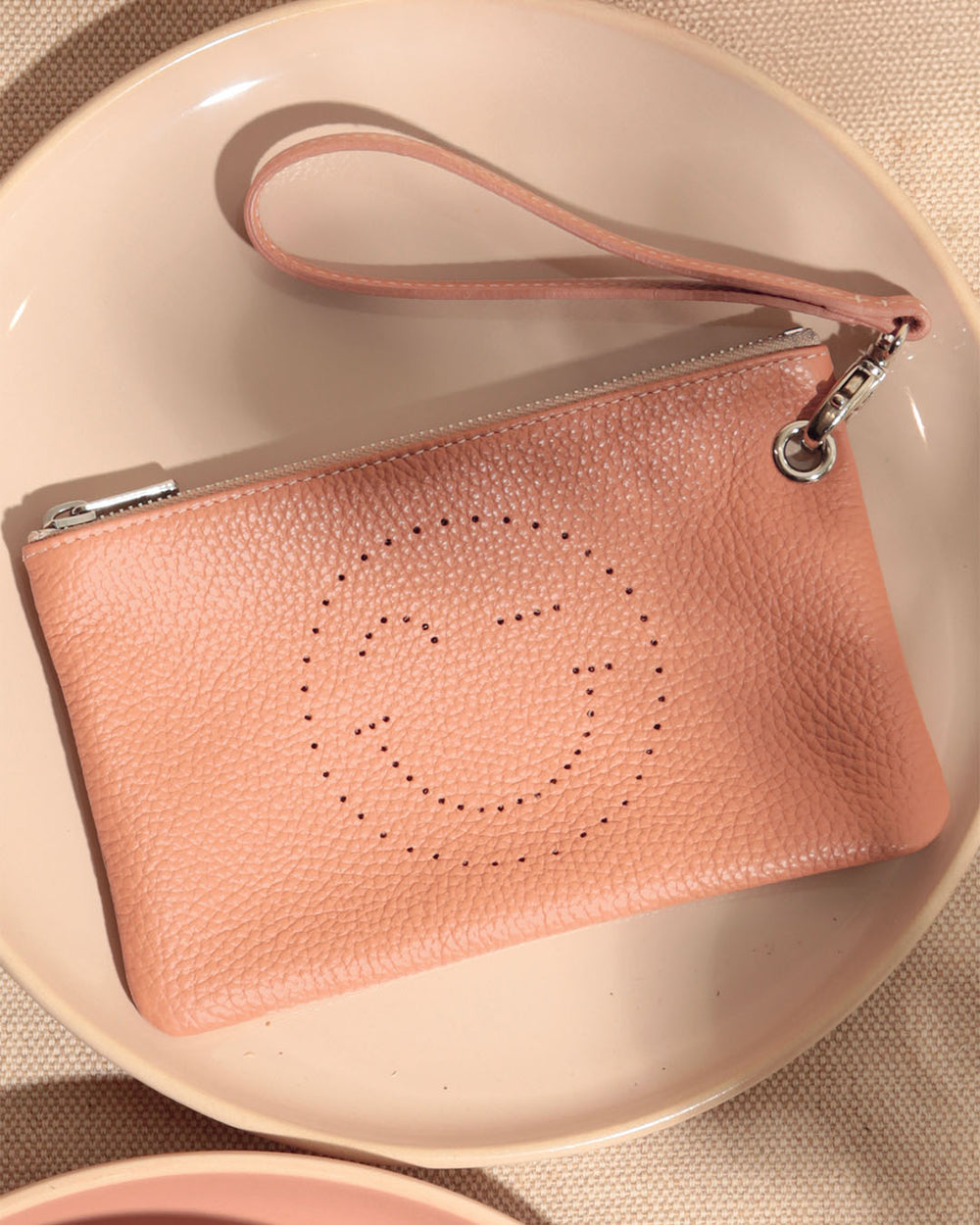 Notre pochette Smiley Renouard en cuir façon vigogne pêche, vue de face en ambiance.