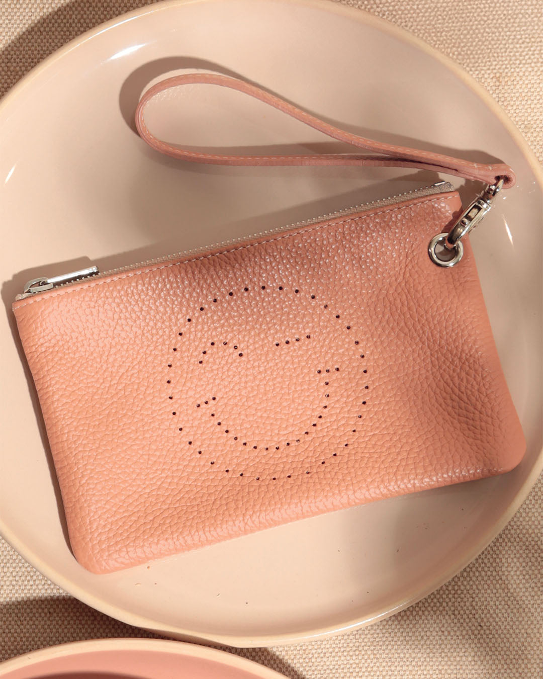 Notre pochette Smiley Renouard en cuir façon vigogne pêche, vue de face en ambiance.