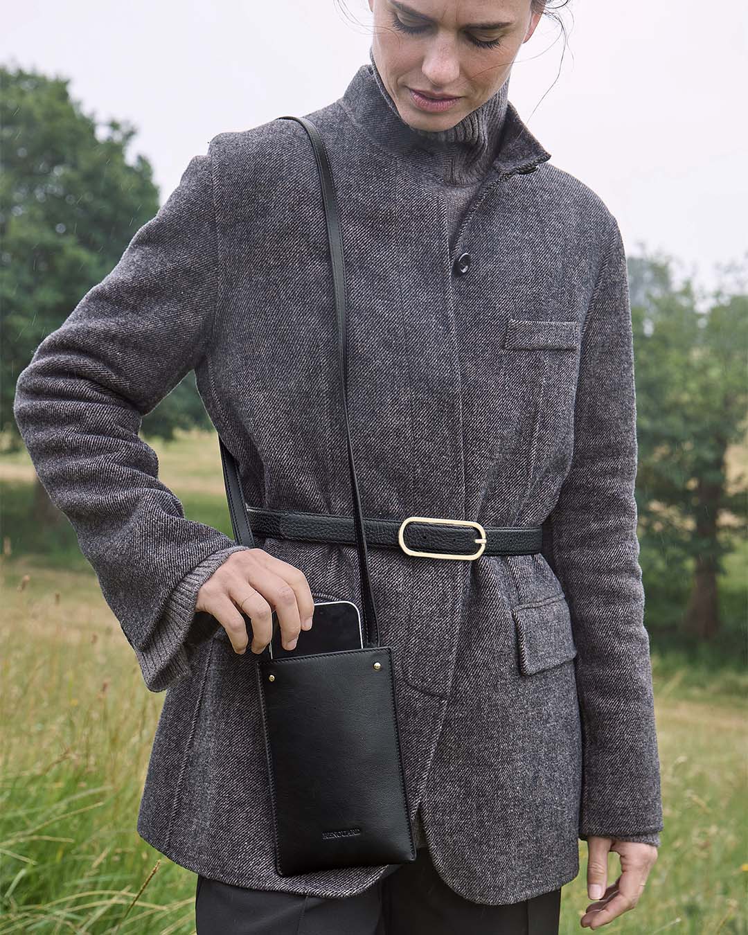 La pochette Téléphone Renouard en cuir lisse noir et accessoires dorés, vue portée par notre mannequin.