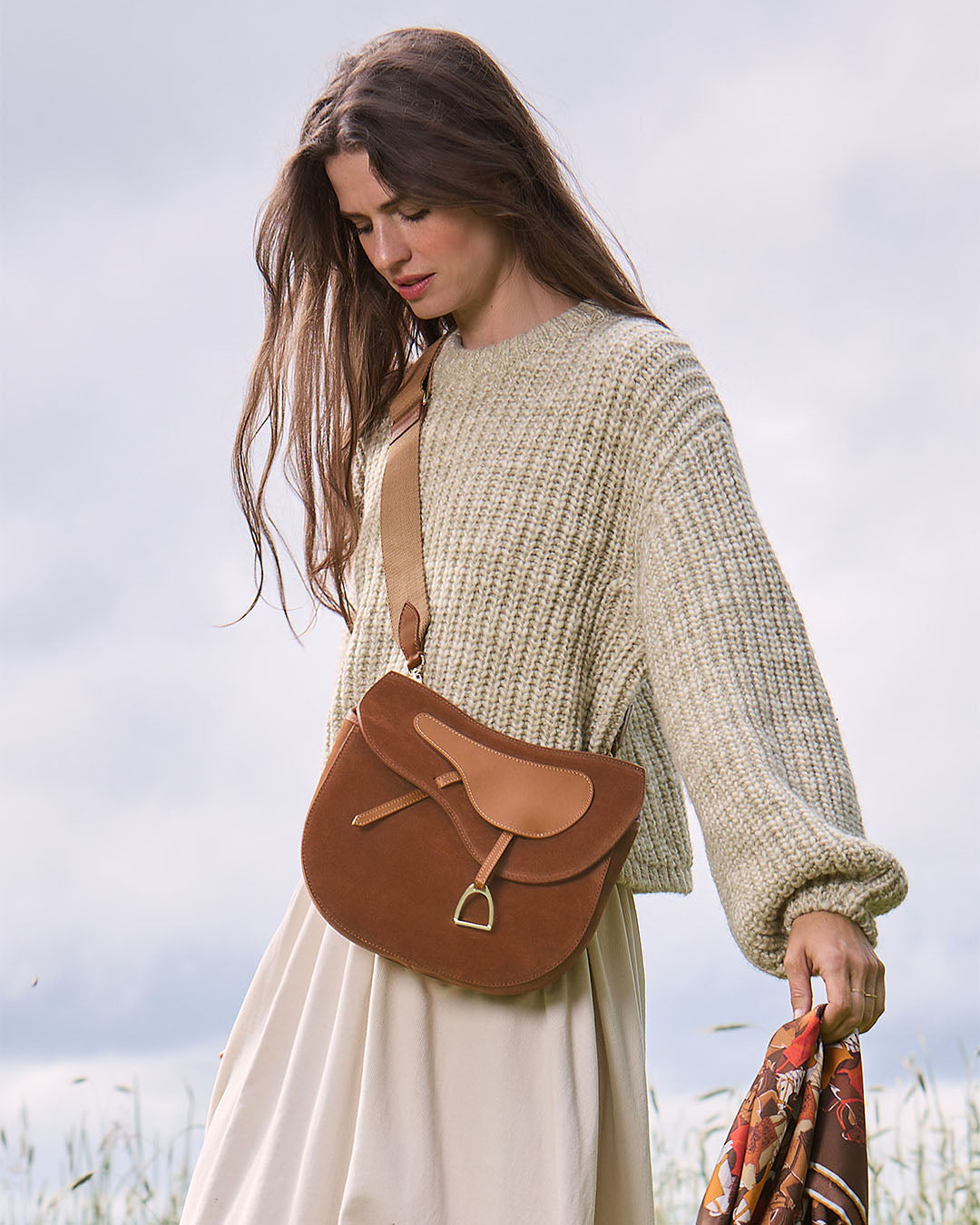 Le sac Cavalerie Renouard en cuir veau velours noisette, cuir lisse camel et sa bandoulière coton camel ; vu porté par notre mannequin.