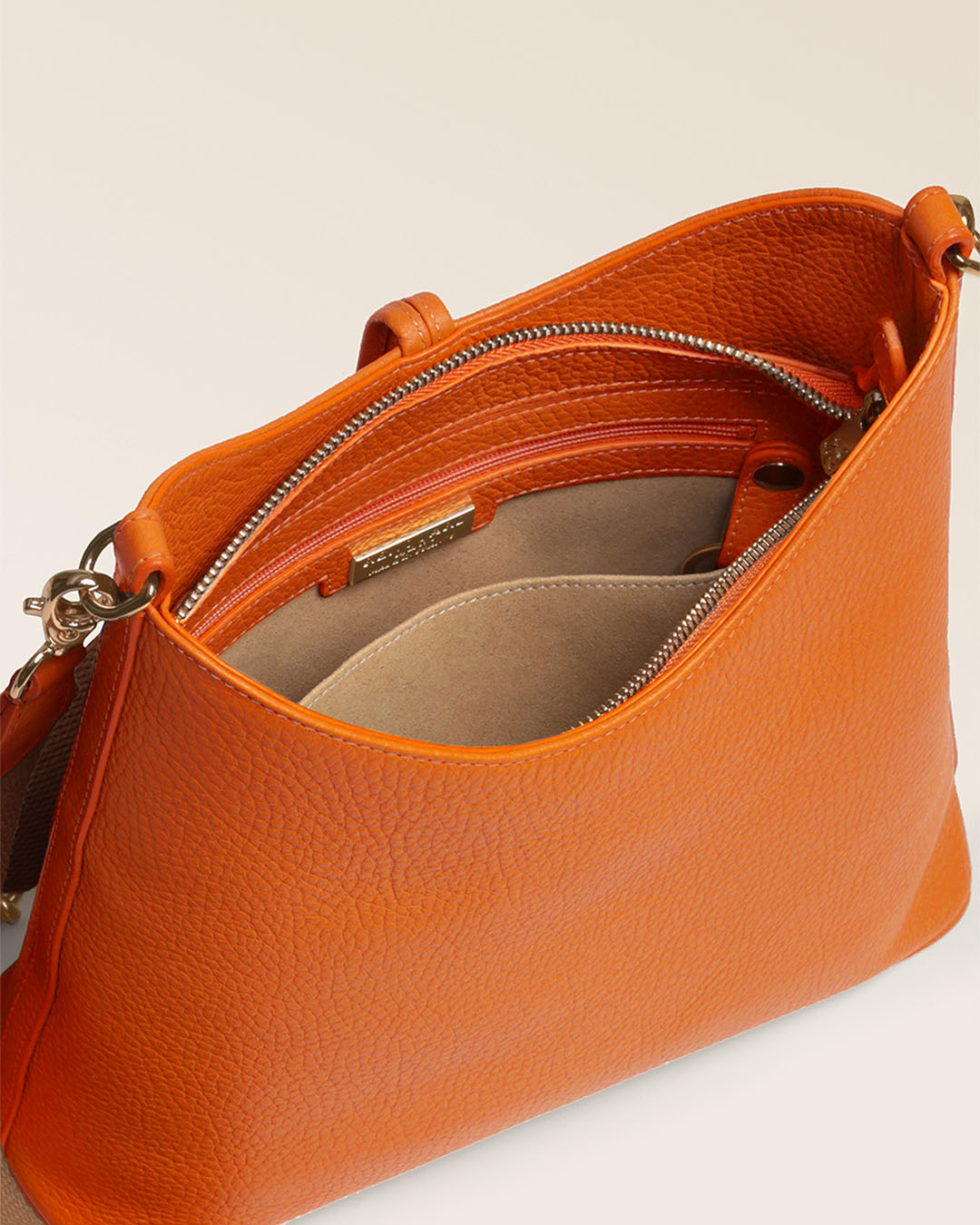 Notre sac Cob Renouard dans sa version Petit modèle, en cuir façon vigogne orange, accessoires dorés et bandoulière coton ; vu du dessus en studio.