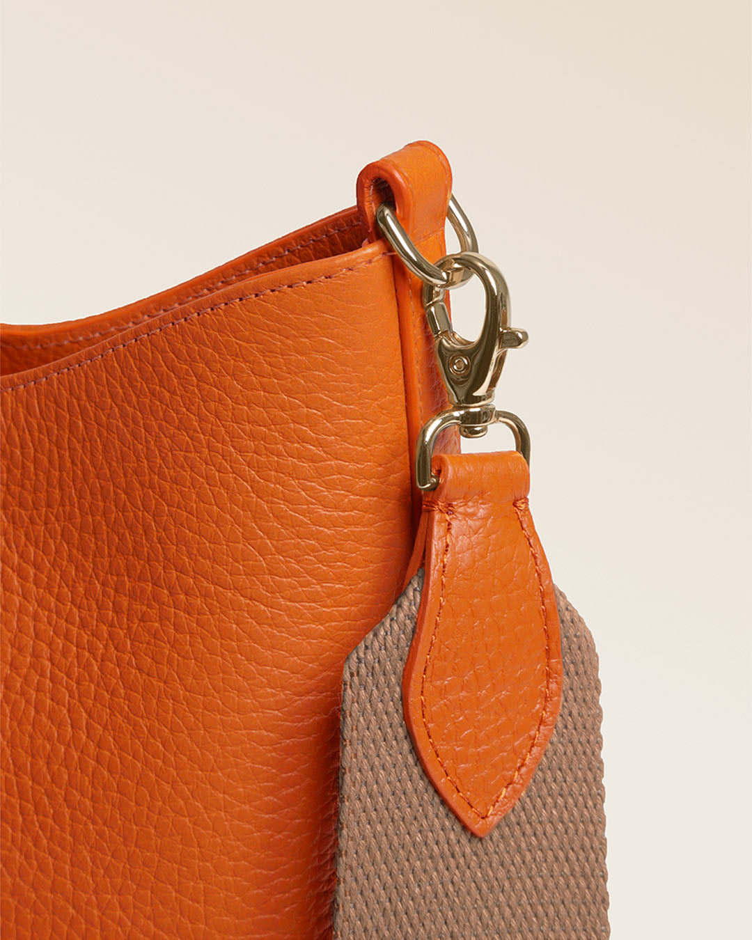 Notre sac Cob Renouard dans sa version Petit modèle, en cuir façon vigogne orange, accessoires dorés et bandoulière coton ; vu de près en studio.