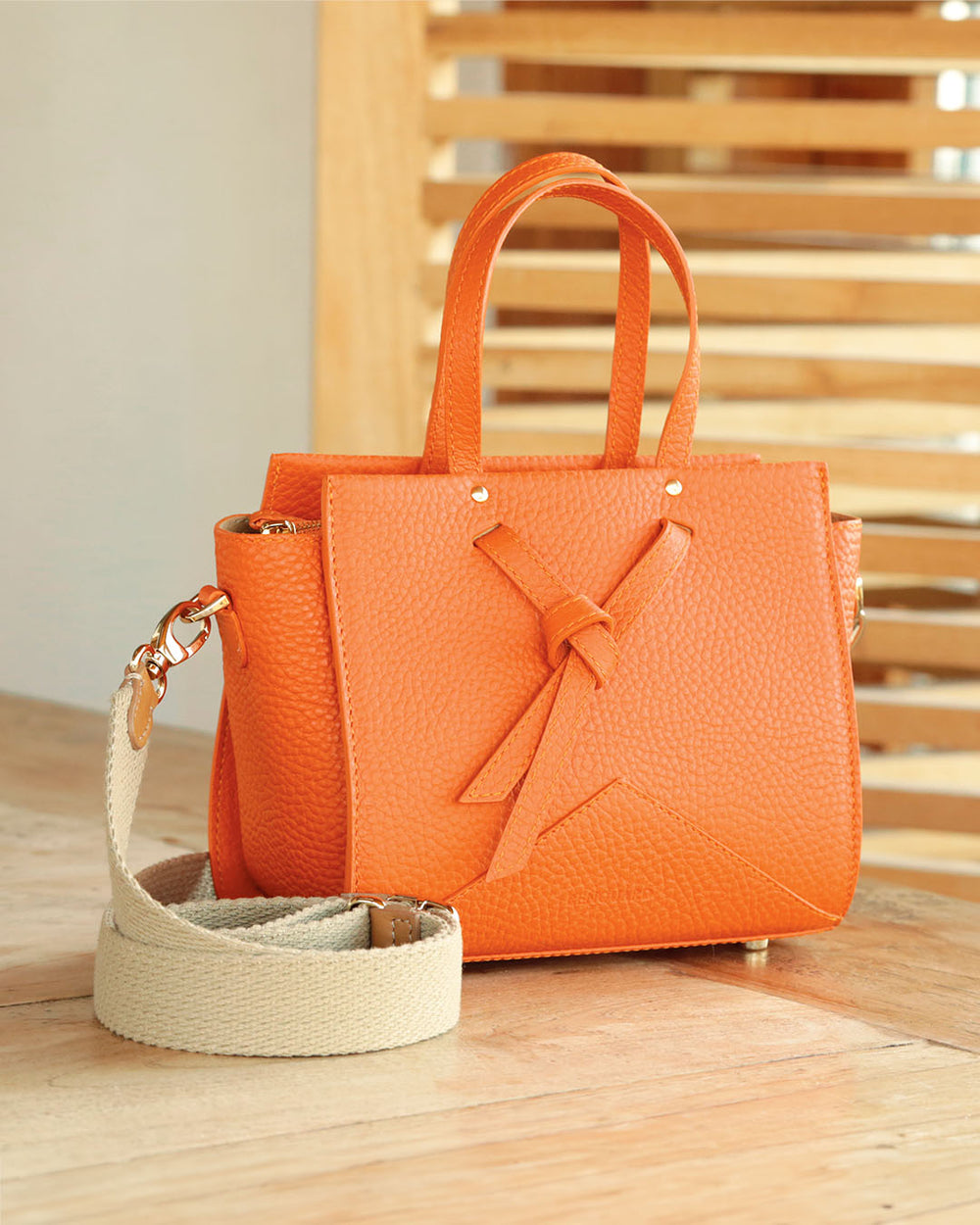 Notre sac Croisière en cuir façon vigogne orange et bandoulière coton sable, vu de quart en ambiance.