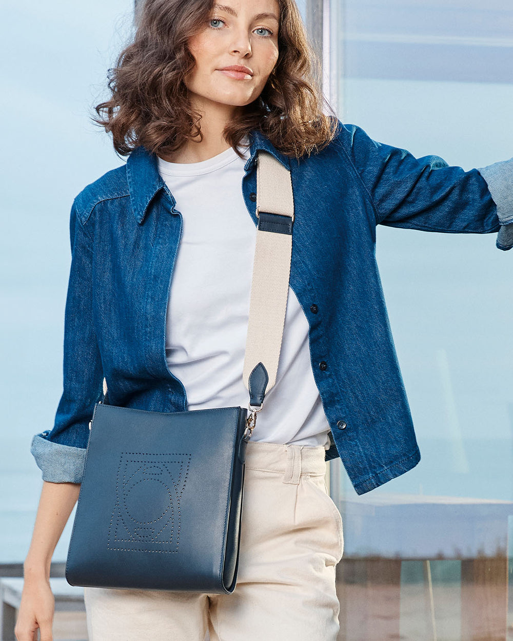 Notre sac Mini Étrivière en cuir lisse marine et bandoulière sangle coton 5cm vu porté par notre mannequin Léa Gouaux. 
