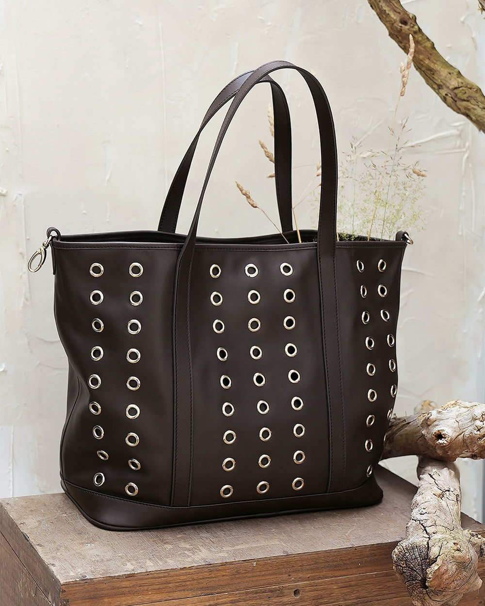 Le sac Zanzibar Renouard en cuir lisse ébène et ses oeillets dorés, vu de face en ambiance.